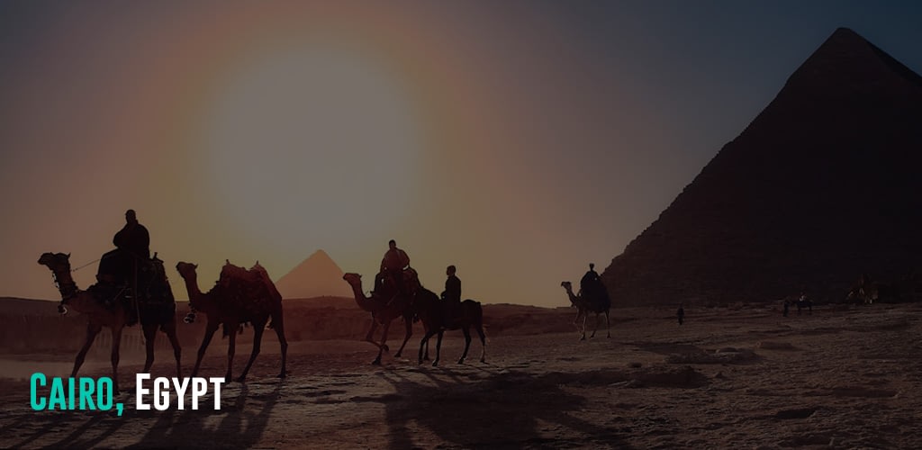 people riding their camels with the pyramid and sunset at the background