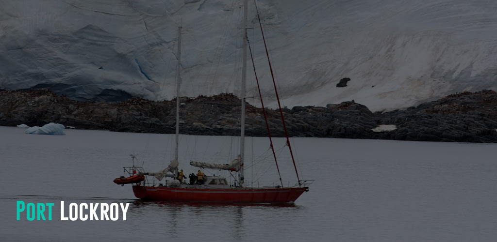 a sailboat anchored in Port Lockroy Bay with a colony of penguins at the background